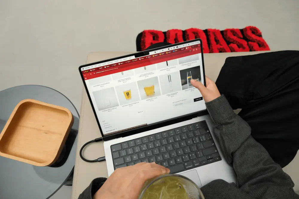 A woman sitting comfortably, using her finger to scroll through an online store directly on her MacBook screen with the laptop on her lap.